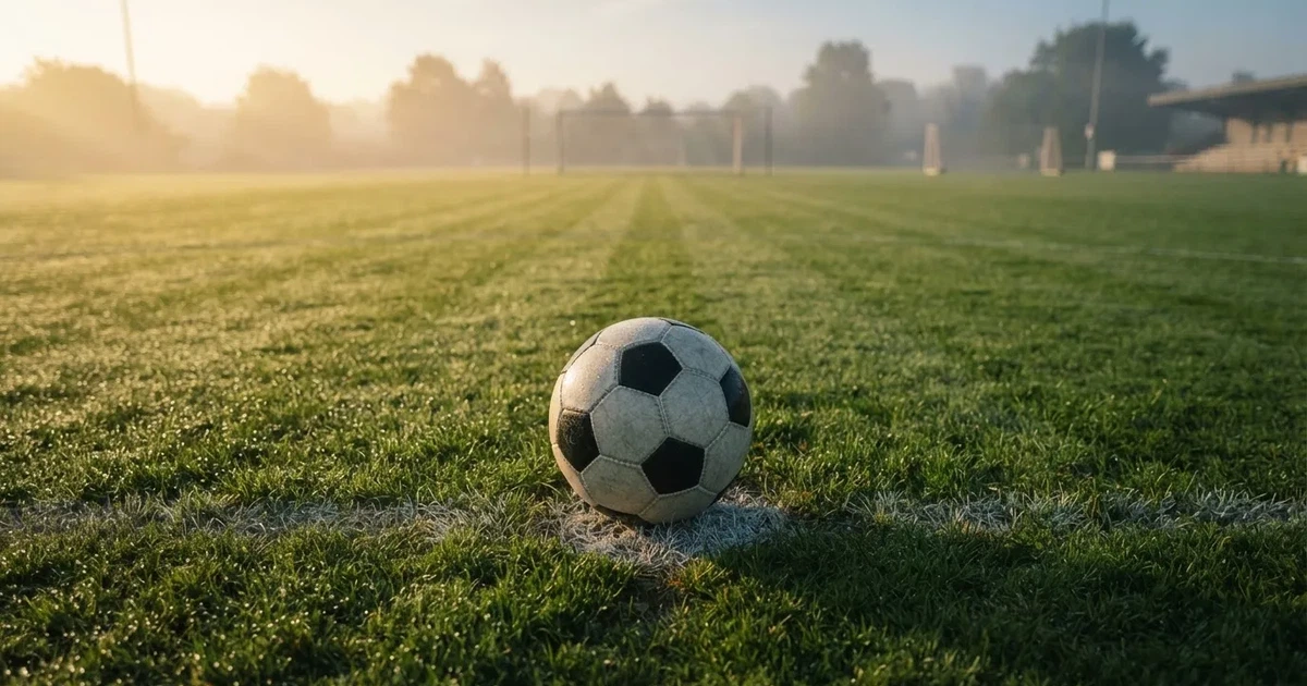 Een voetbal op de middenstip van een grasveld in het ochtendlicht