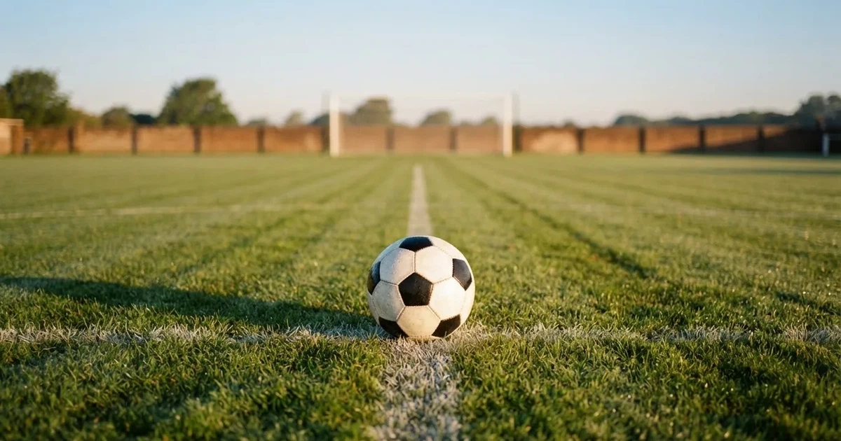Een voetbal op de middenstip van een grasveld in het ochtendlicht
