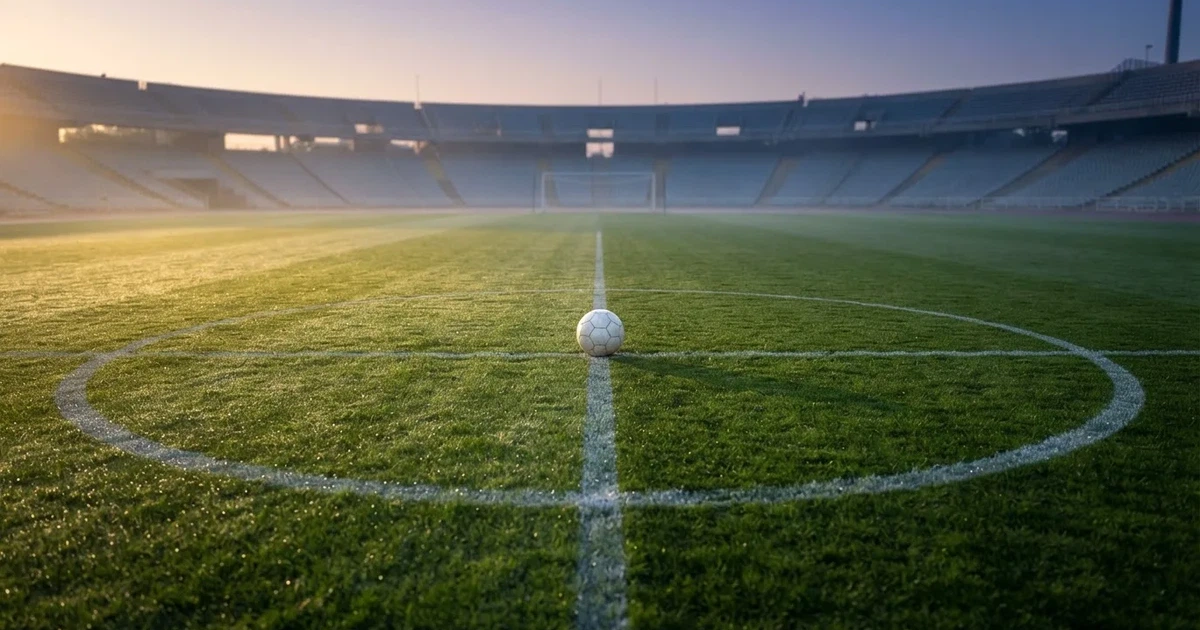 Een voetbal op de middenstip van een grasveld in het ochtendlicht