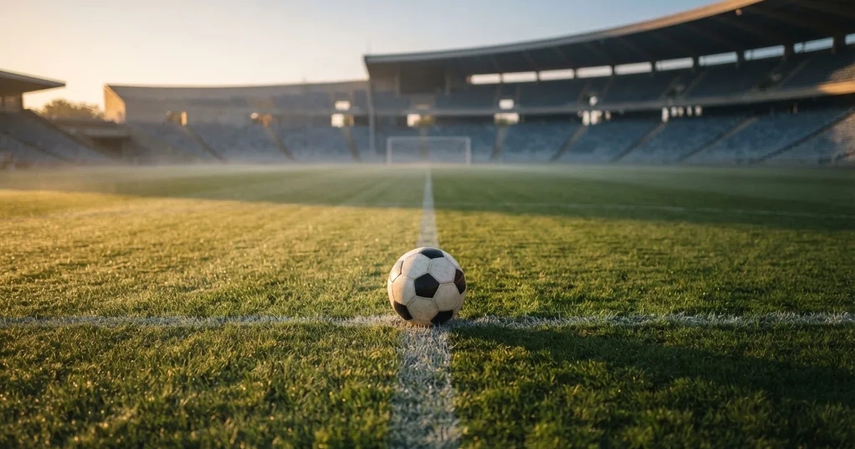 Een voetbal op de middenstip van een grasveld in het ochtendlicht