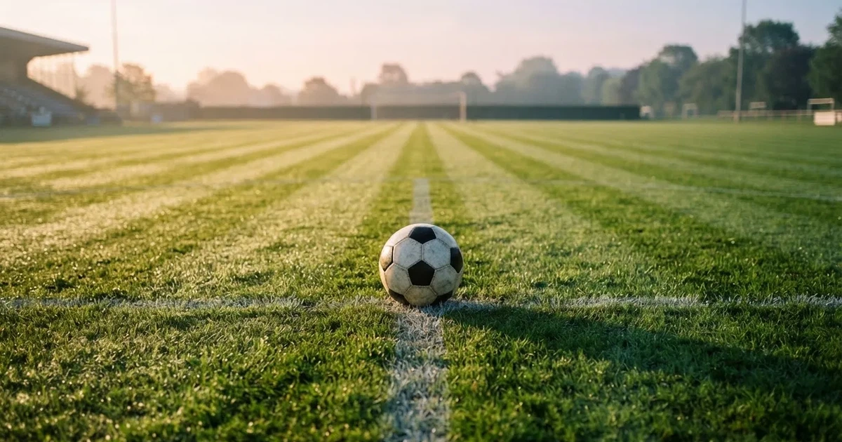 Een voetbal op de middenstip van een grasveld in het ochtendlicht