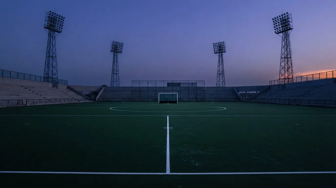Een leeg voetbalstadion met lichtmasten bij schemering