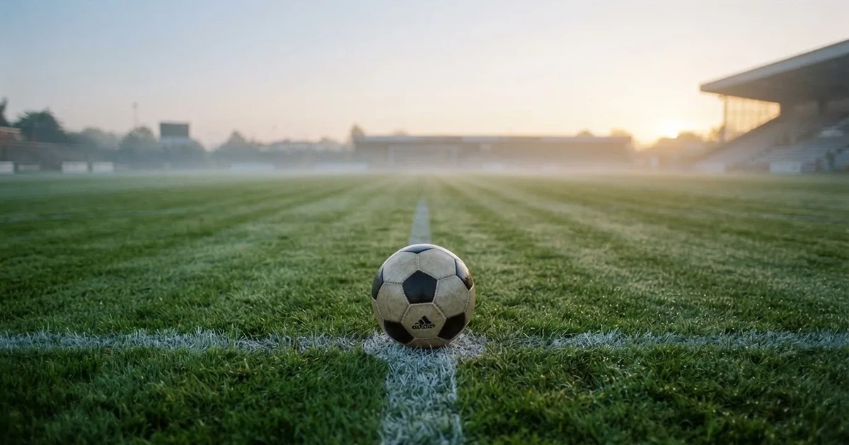 Een voetbal op de middenstip van een grasveld in het ochtendlicht
