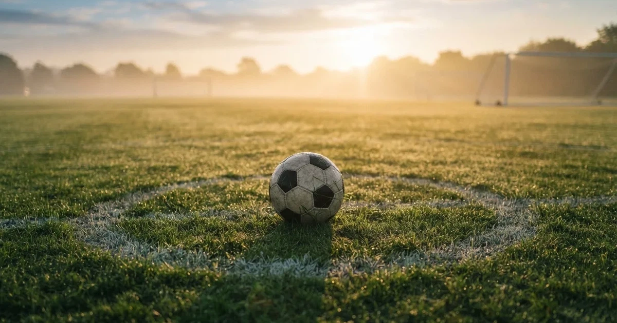 Een voetbal op de middenstip van een grasveld in het ochtendlicht